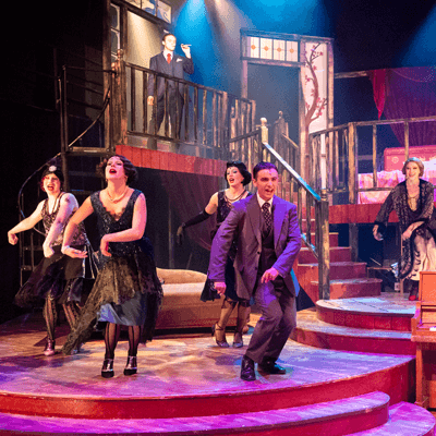 Actors in period costume dance on the stage.